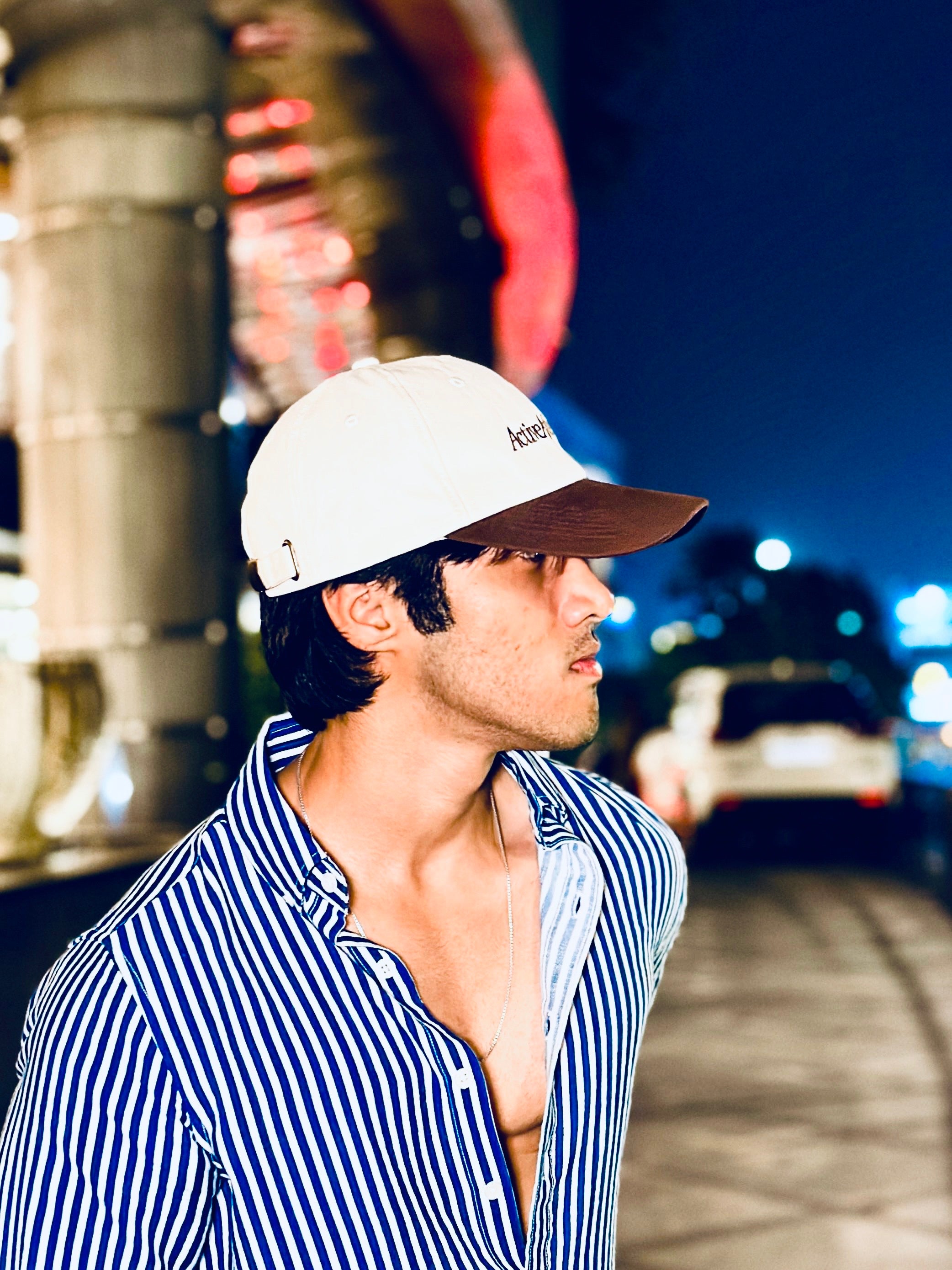 Man wearing a white cap and striped shirt in an urban setting at night.