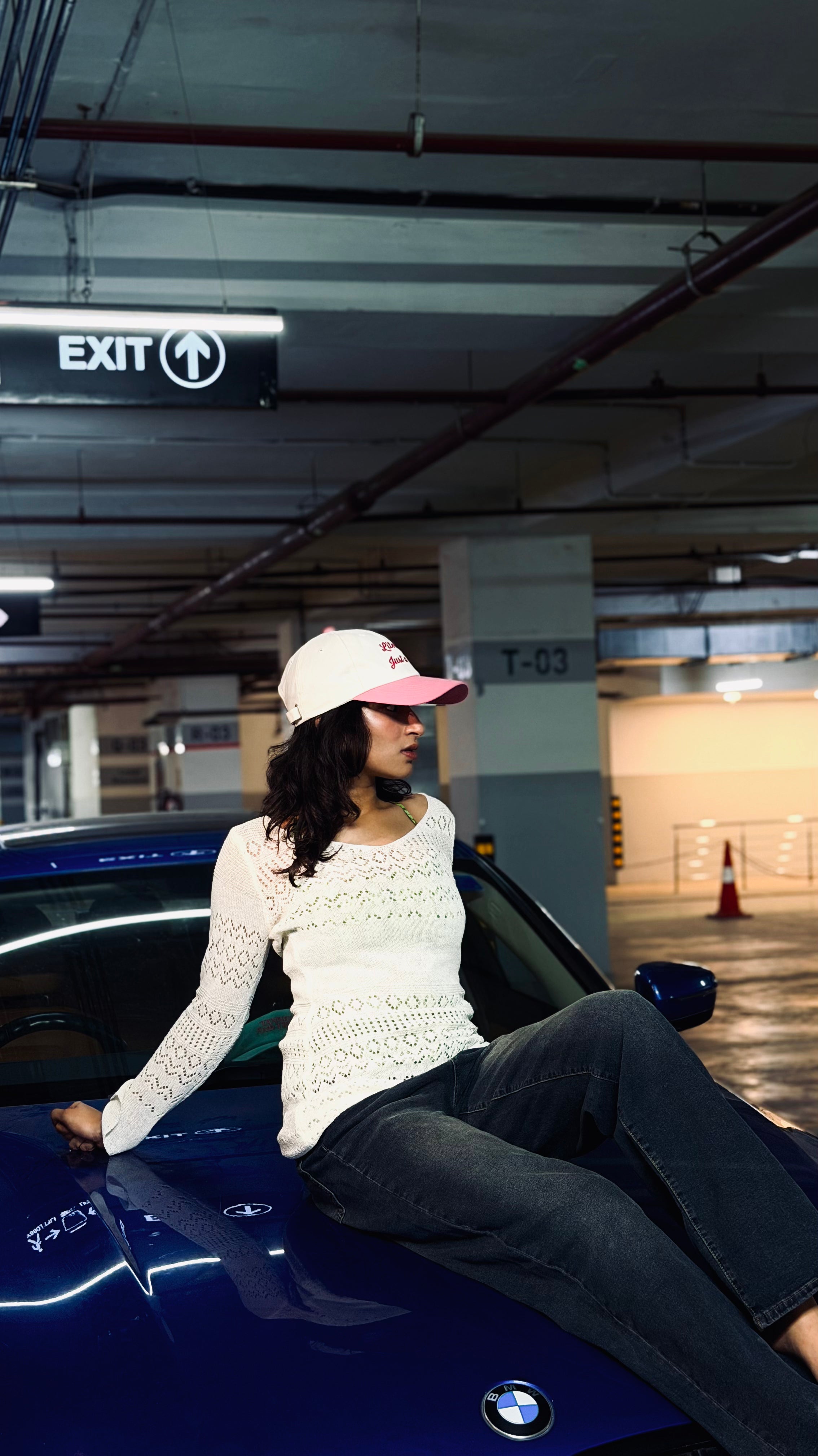 Woman sitting on a blue car in a parking garage