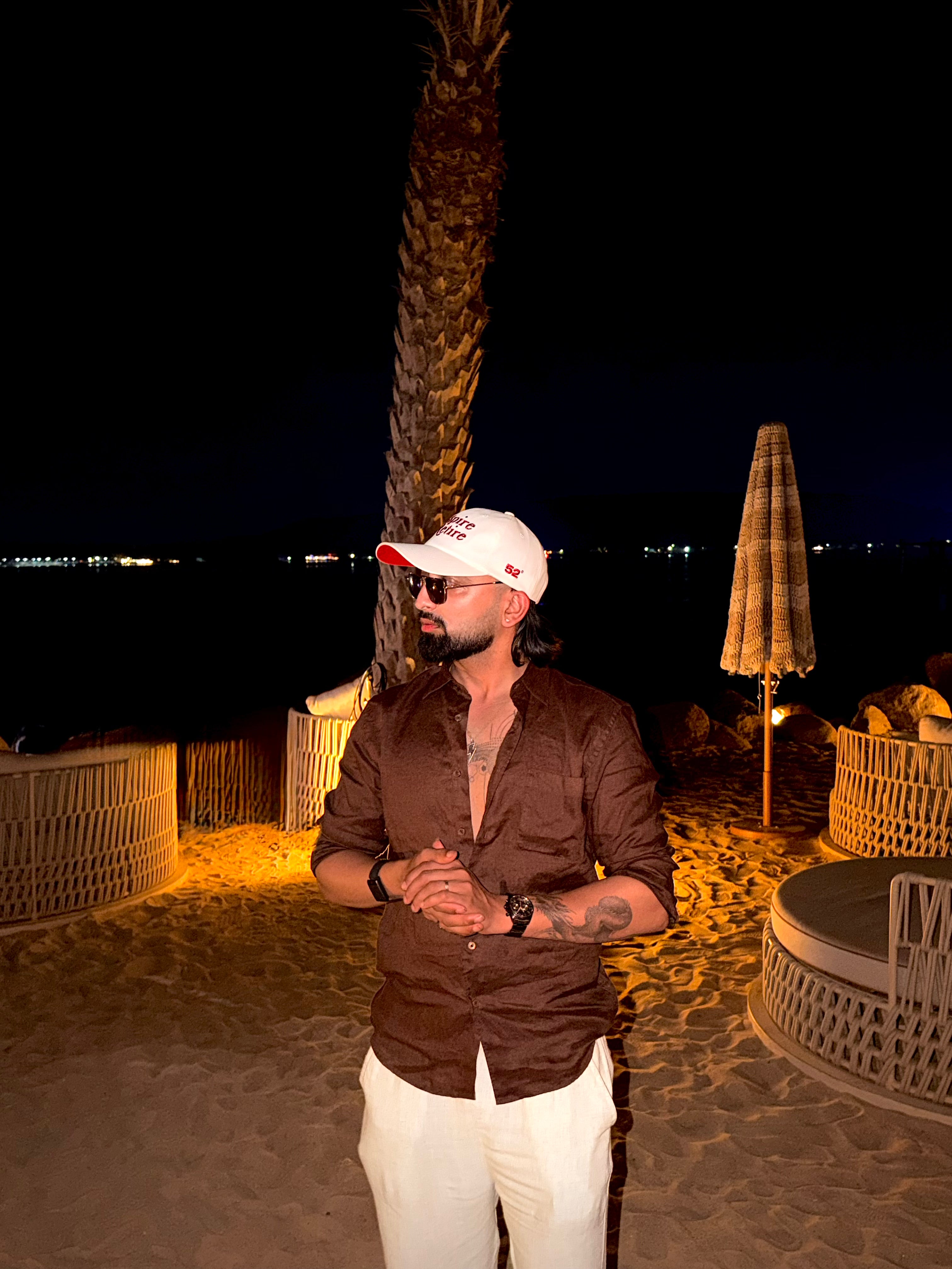 Man standing on a beach at night with palm trees and umbrellas in the background