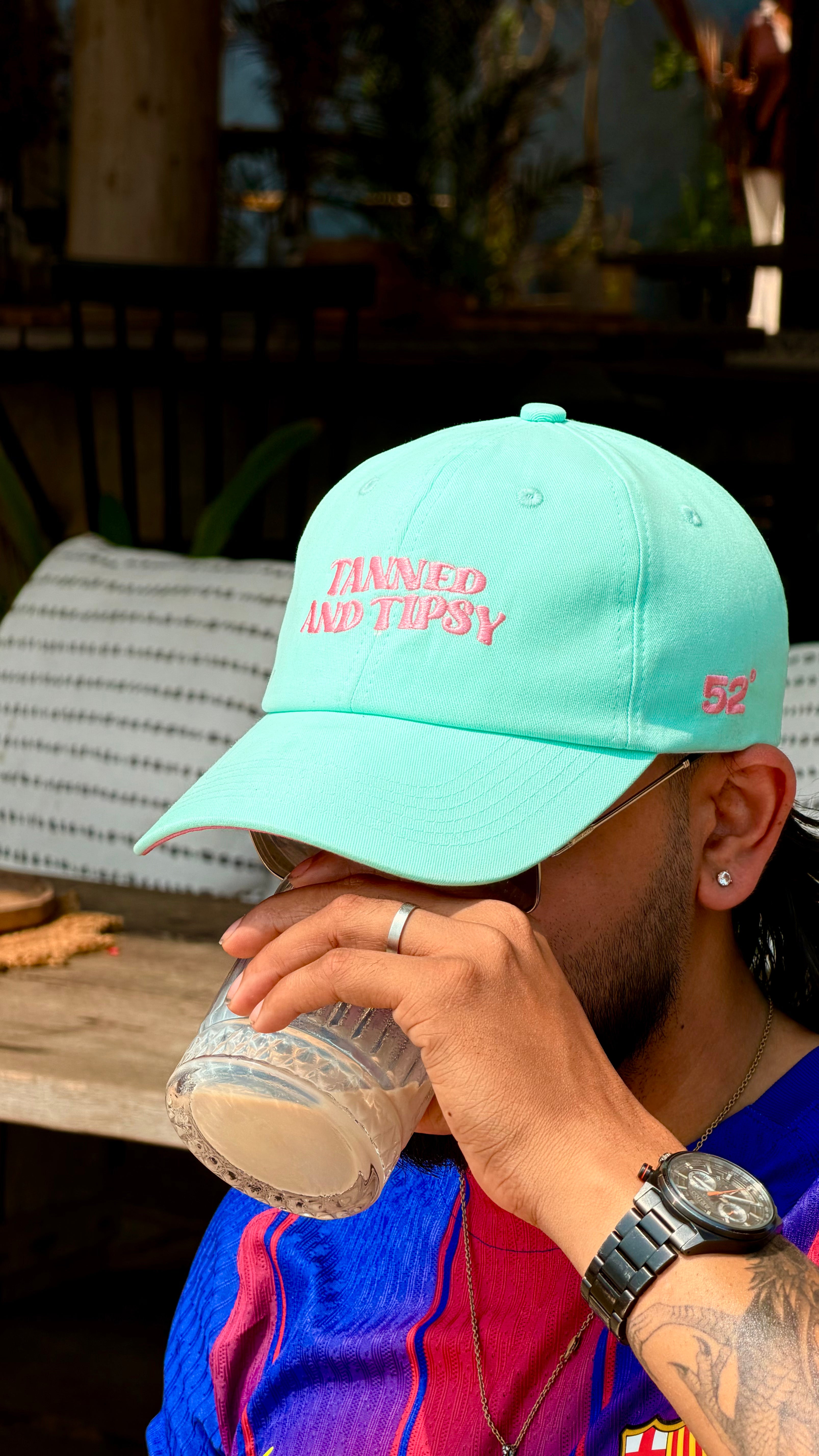 Person wearing a turquoise cap with text, drinking from a container outdoors.