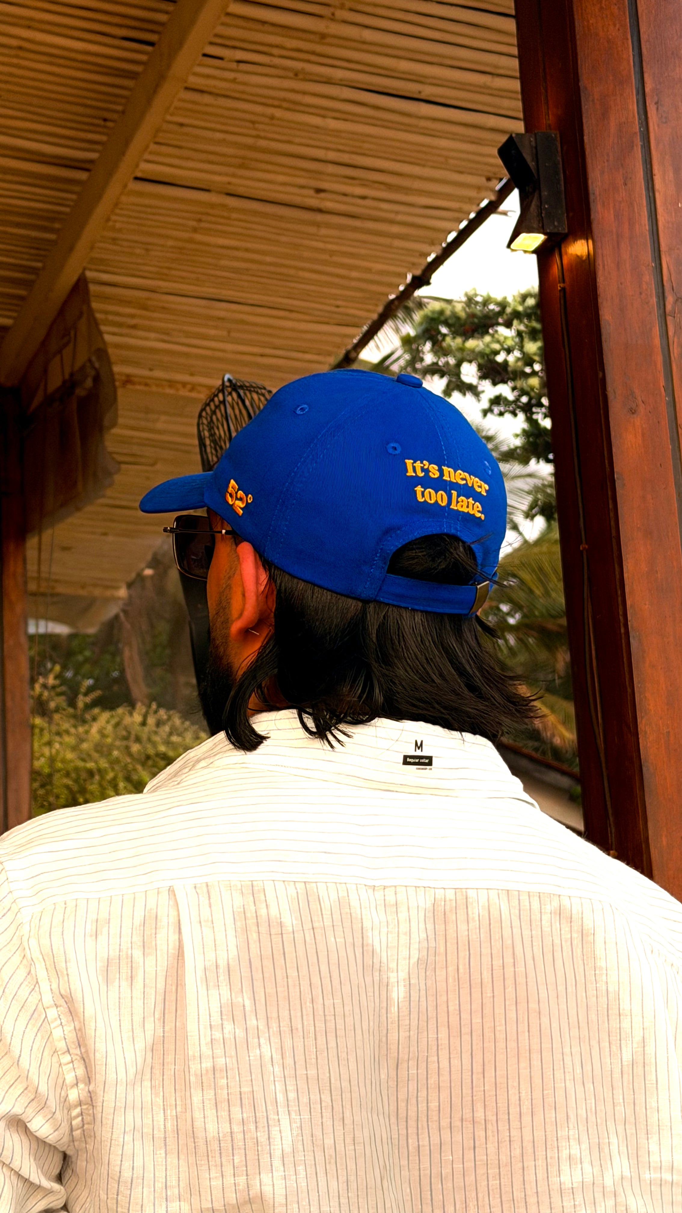 Person wearing a blue cap with text, standing in front of a wooden structure.