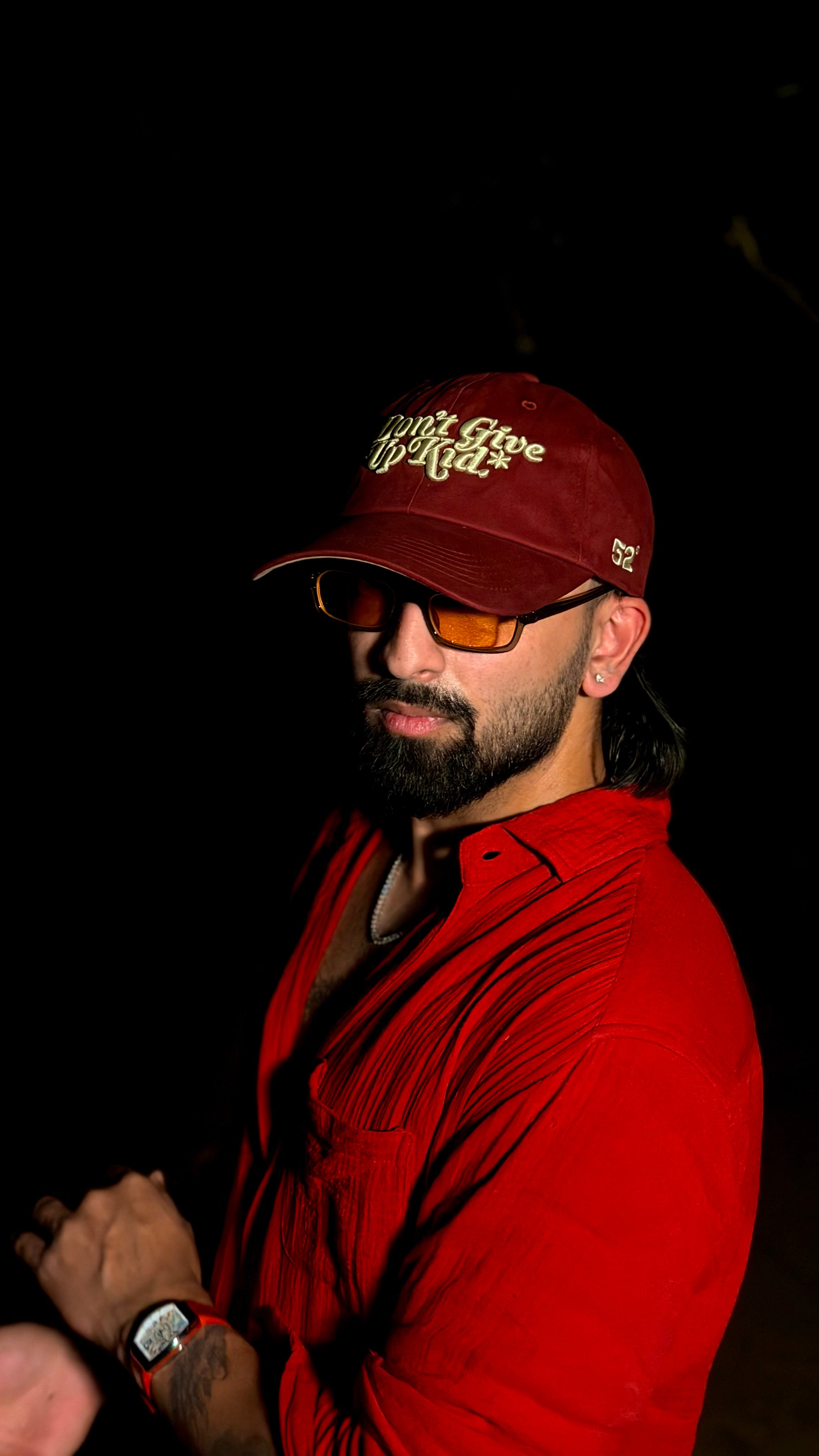 Man wearing a red cap and sunglasses with a dark background