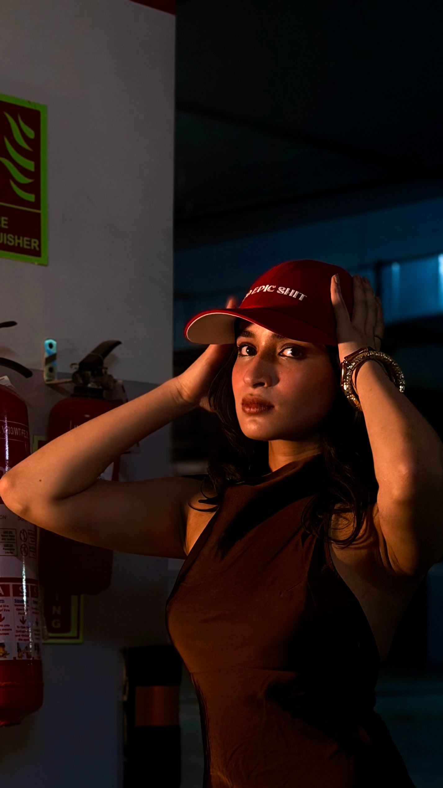 Person wearing a red cap in a dimly lit room with a fire extinguisher visible.