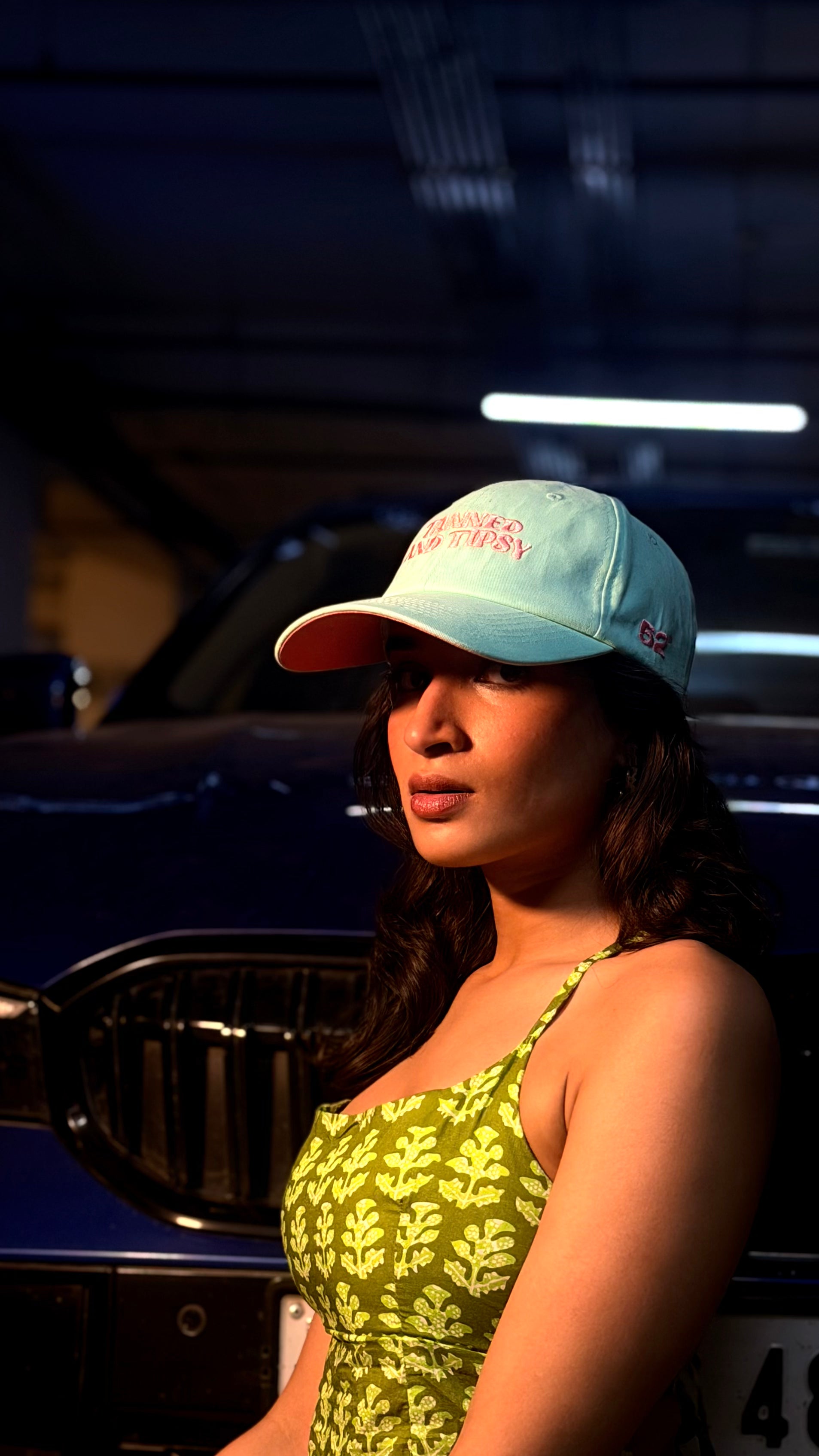 Woman wearing a blue cap and green dress standing in front of a car.