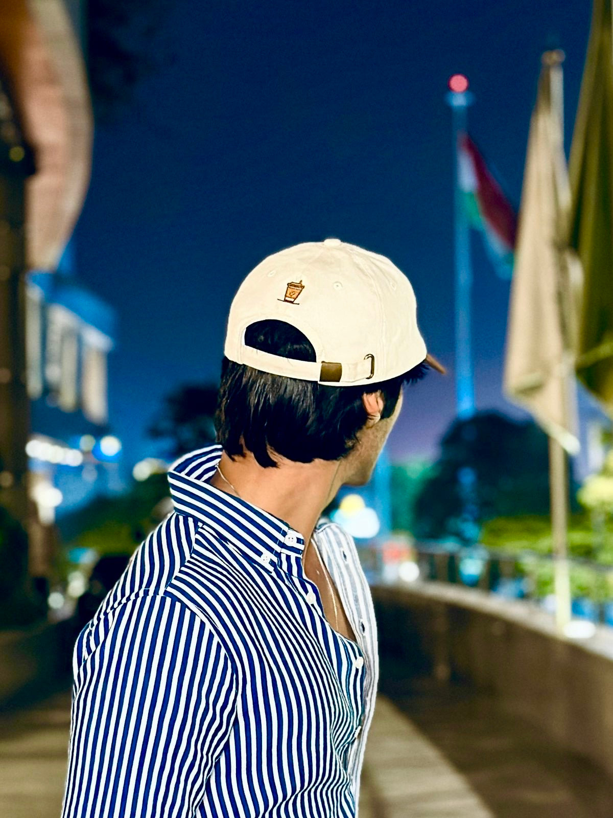 Person wearing a cap and striped shirt with a blurred background of lights and flags