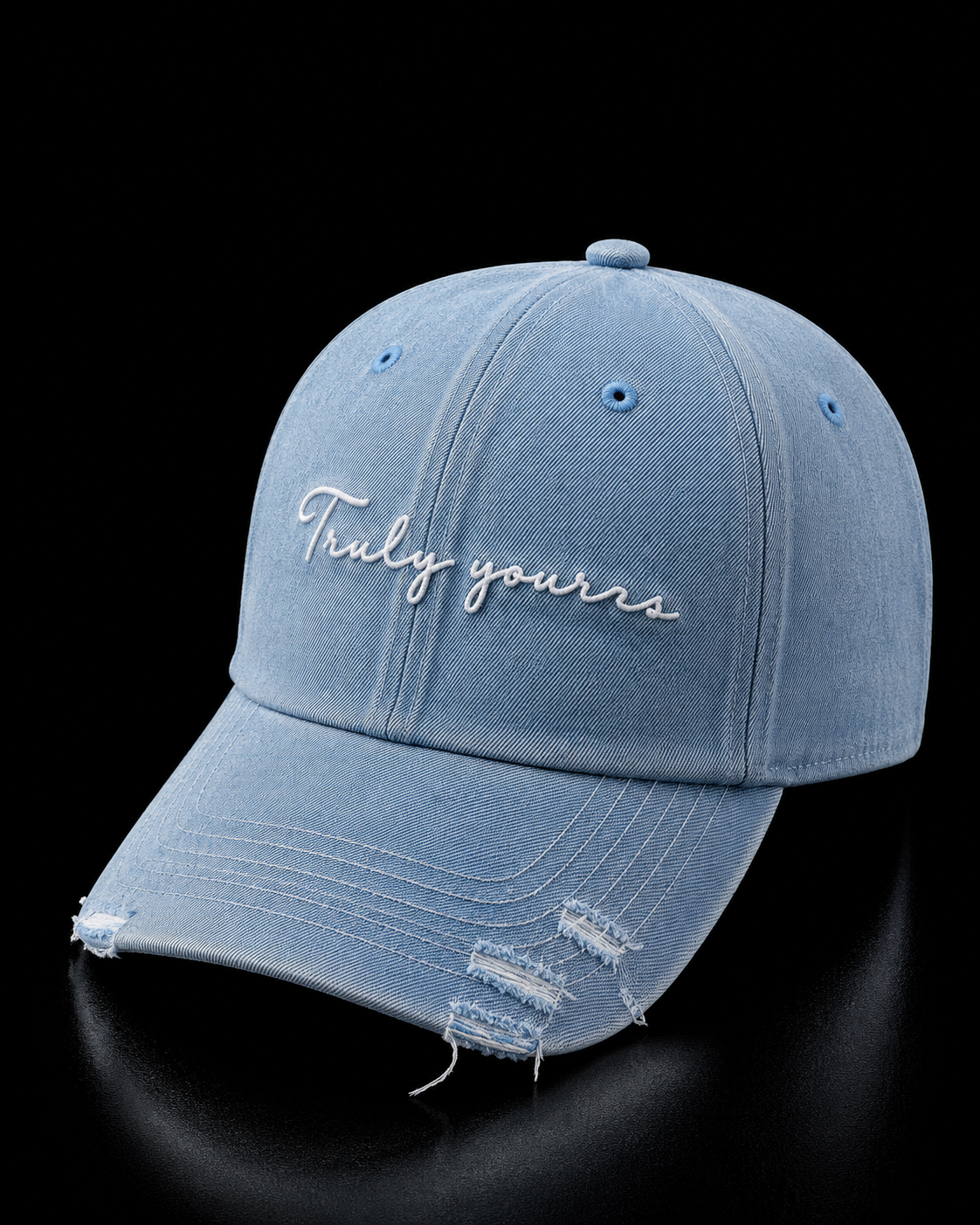 Blue distressed cap with 'Truly yours' embroidery on a black background
