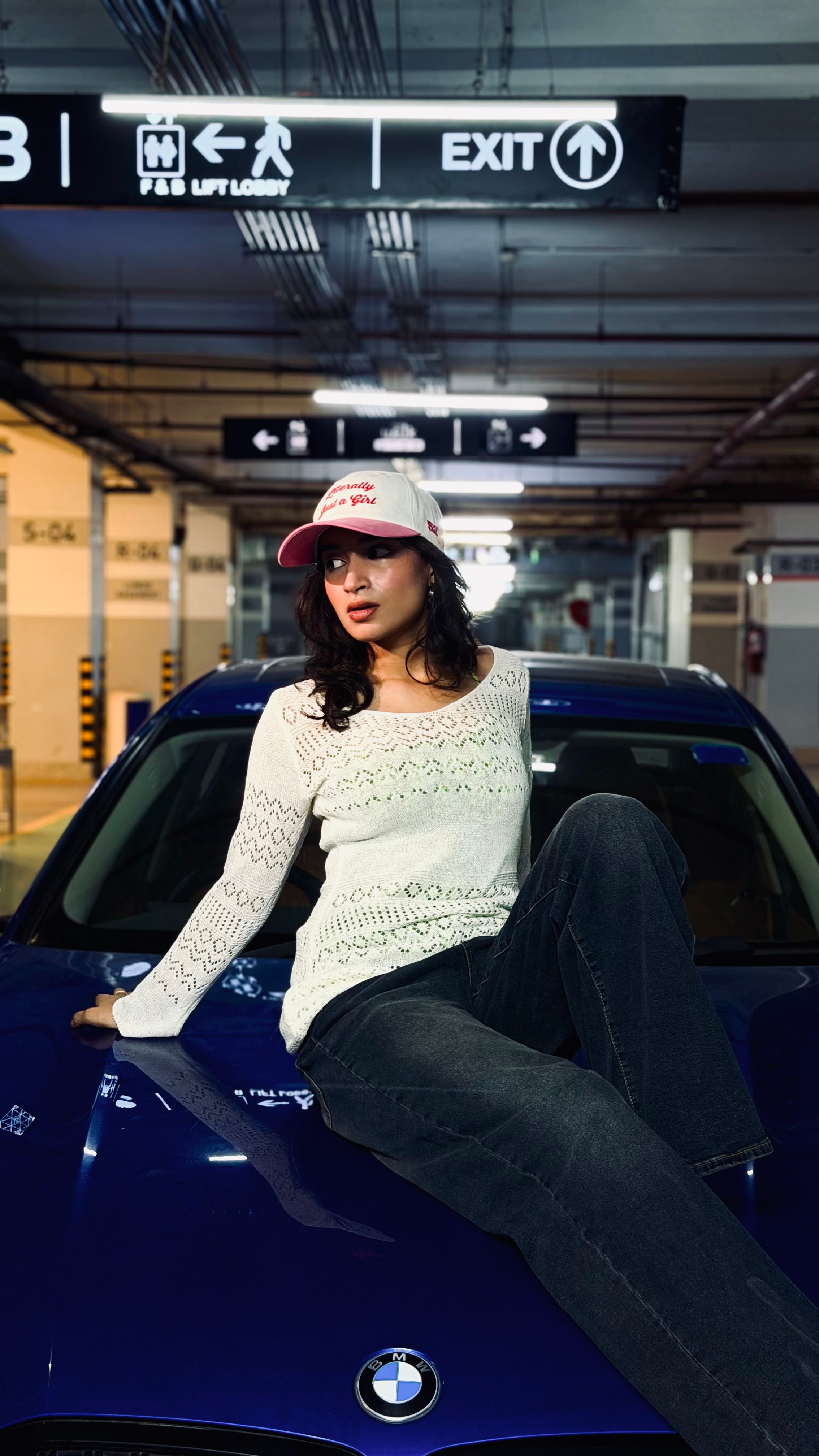 Woman sitting on a blue BMW car in a parking garage
