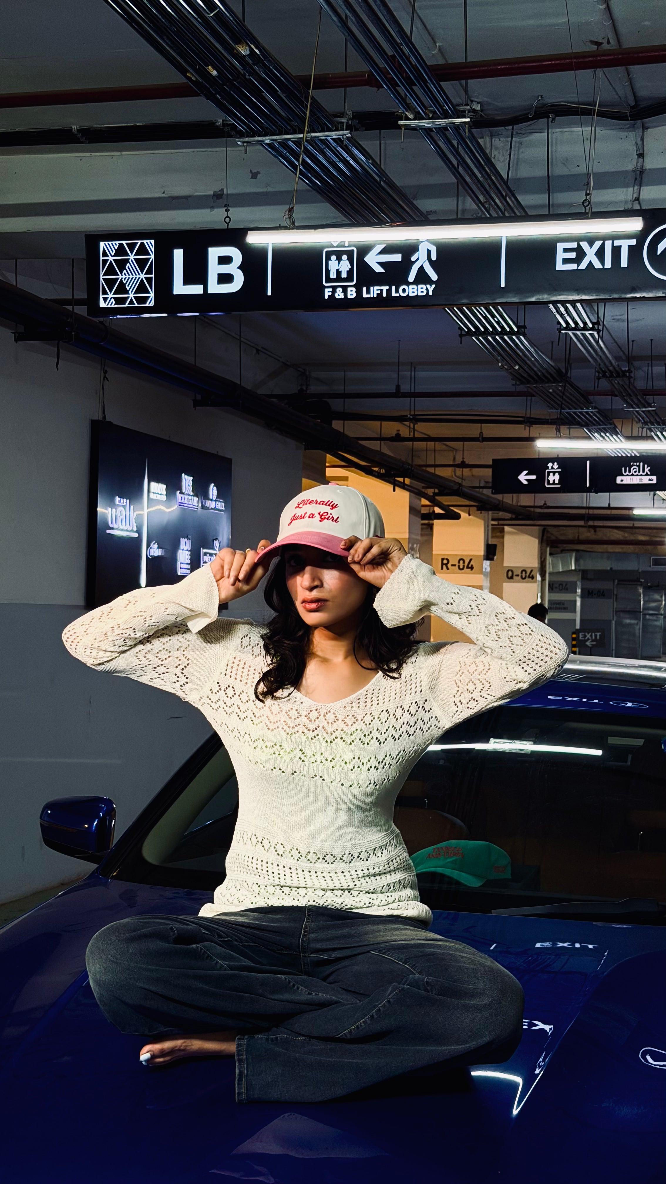 Person sitting on a car in a parking garage with a sign above.