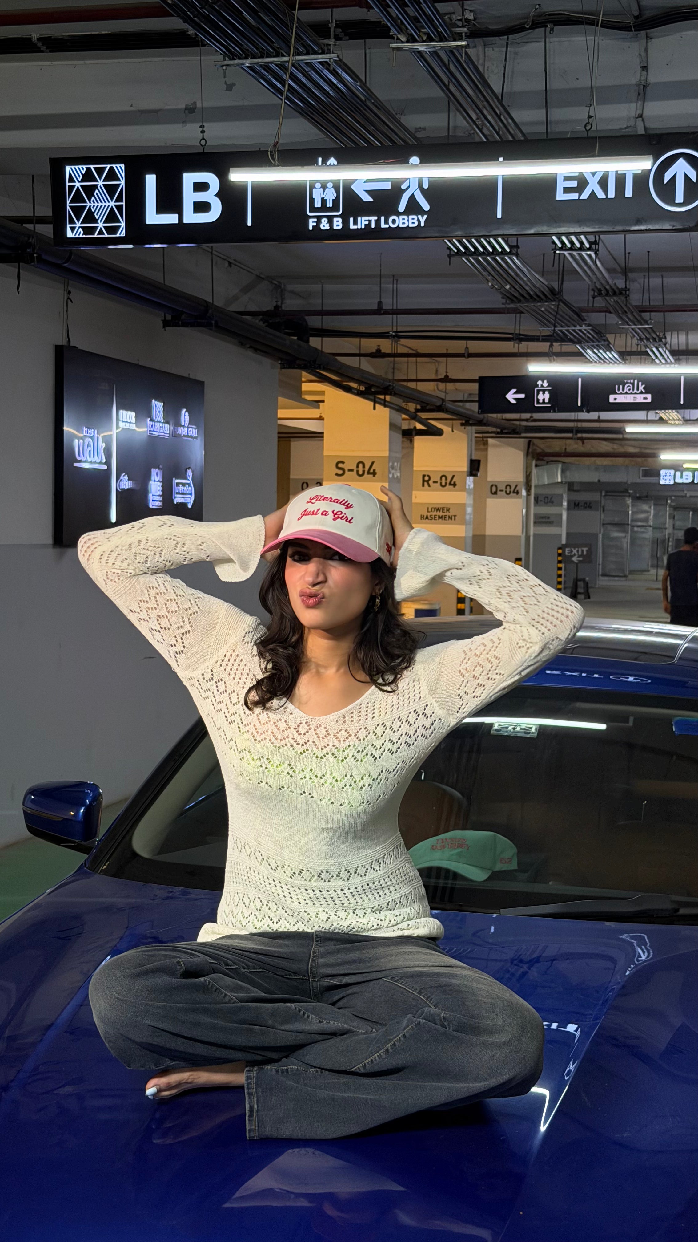 Person sitting on a car in a parking garage with an 'EXIT' sign above.