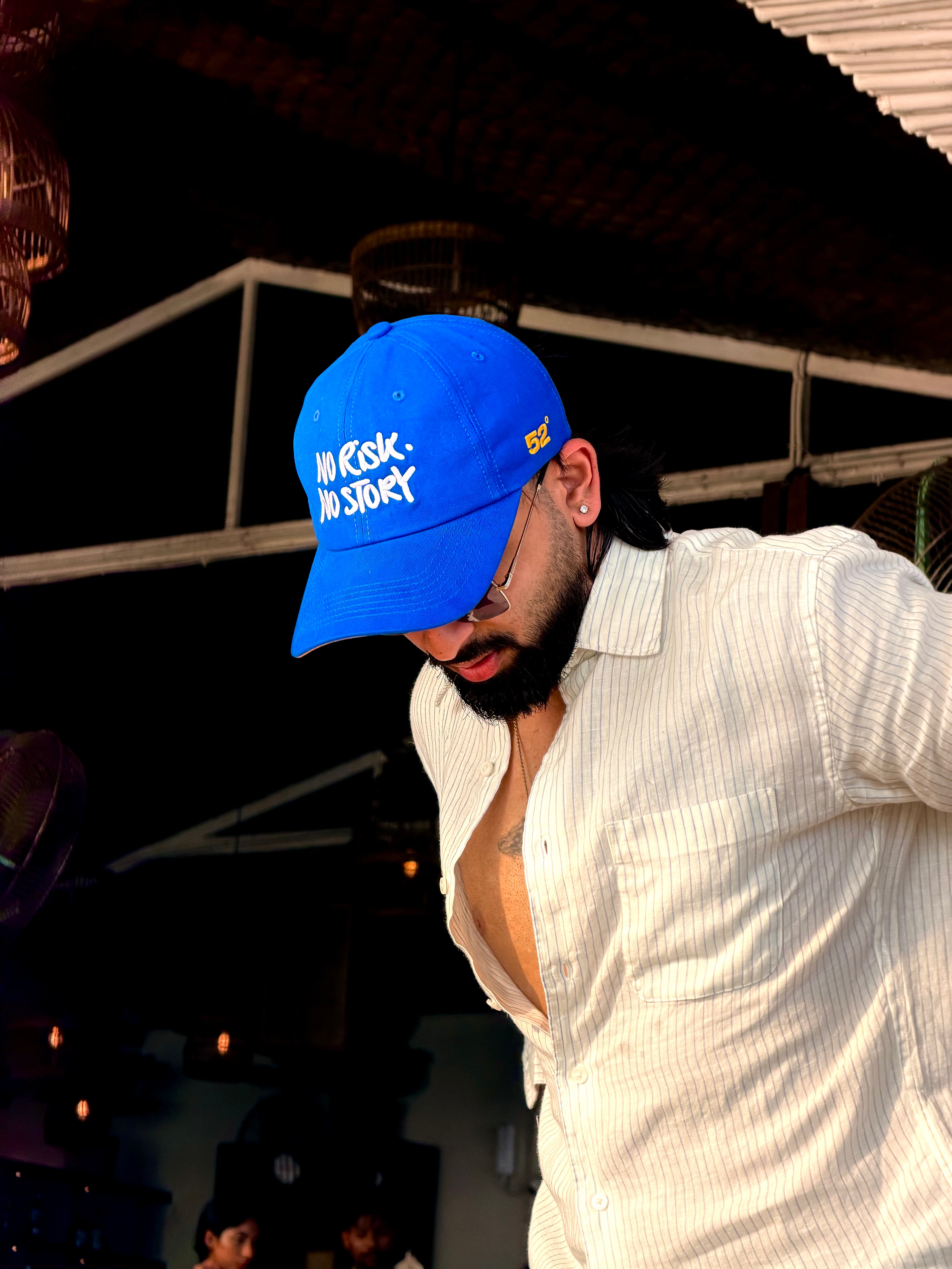 Person wearing a blue cap with text, standing outdoors under a dark roof.