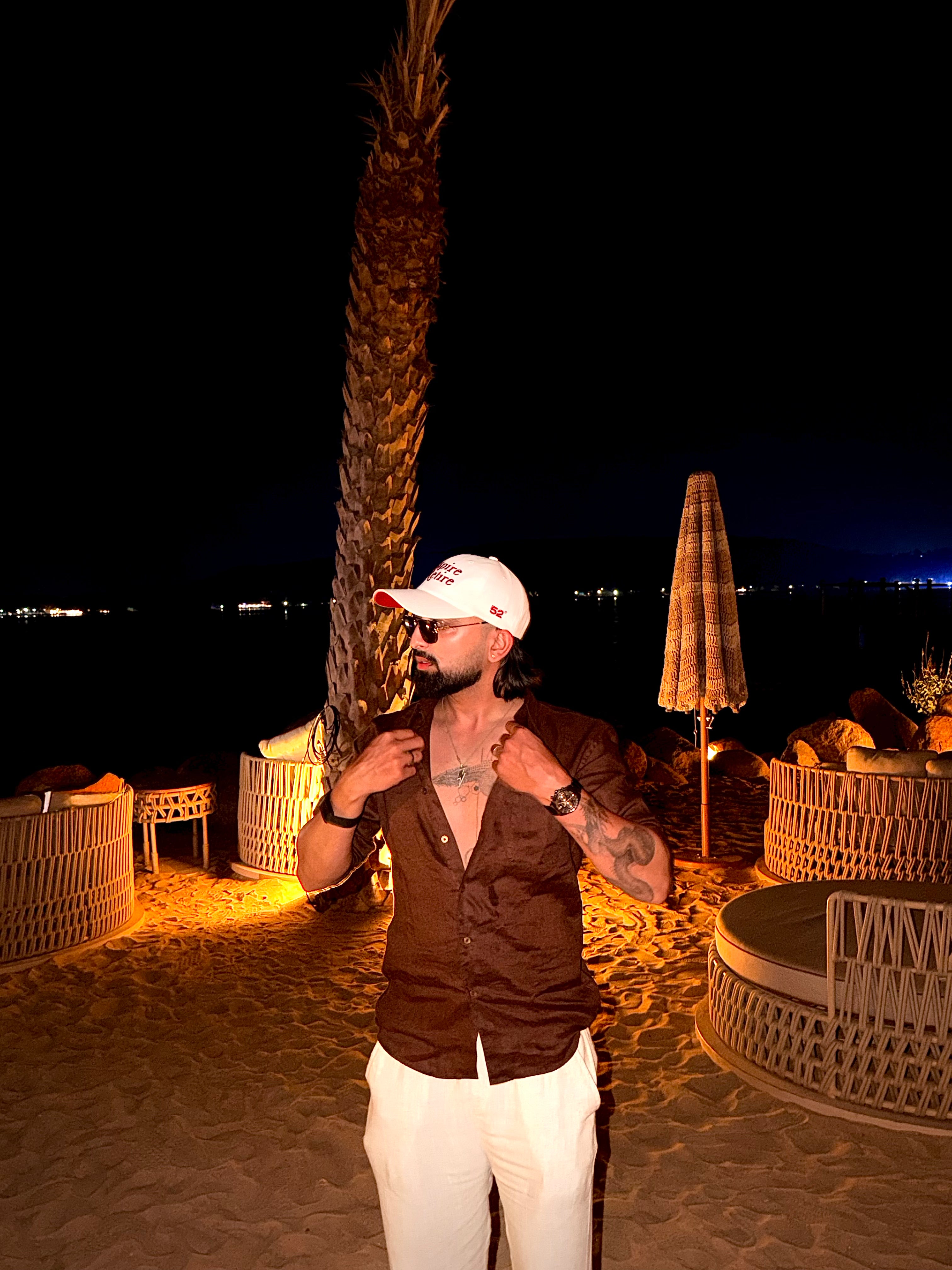 Man standing on a beach at night with palm trees and umbrellas in the background