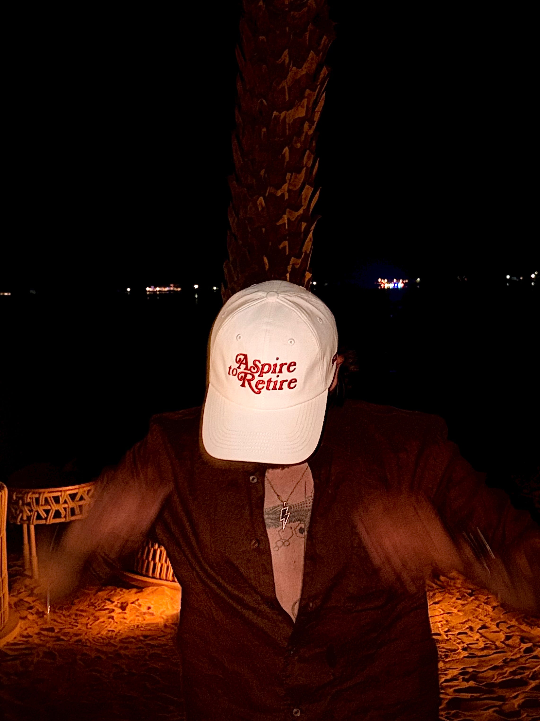 Person wearing a cap with 'Aspire to Retire' text at night.