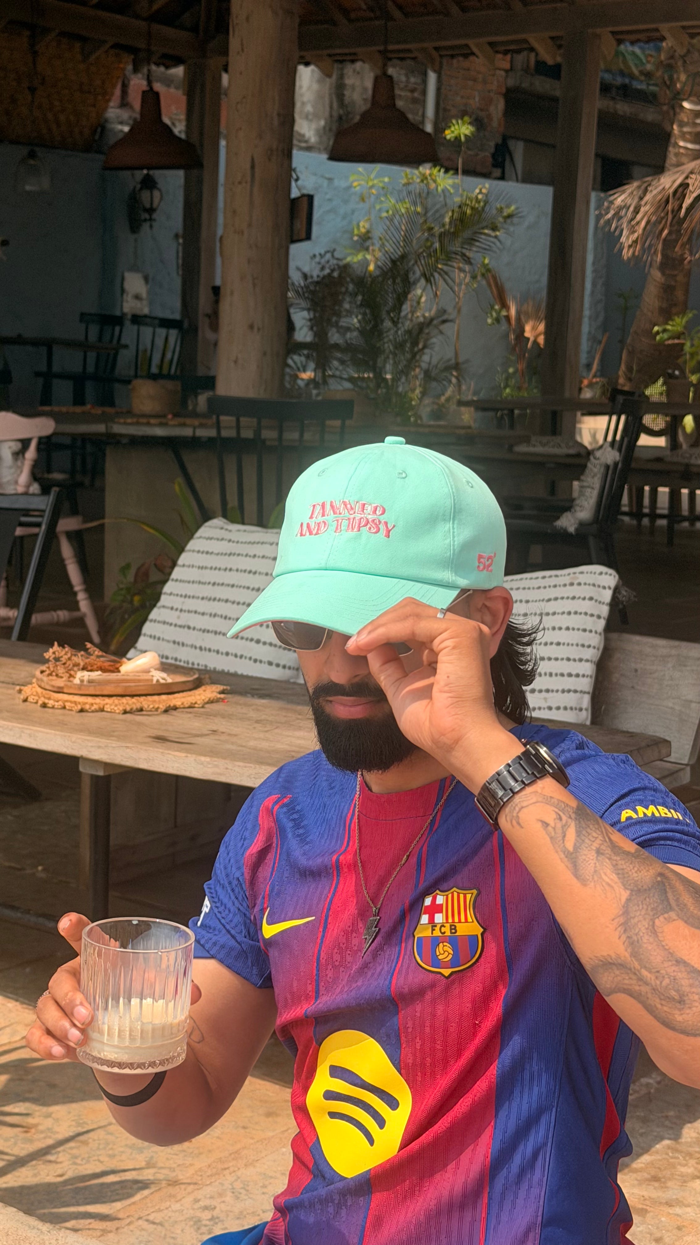 Person wearing a sports jersey and cap, holding a glass, in an outdoor setting.