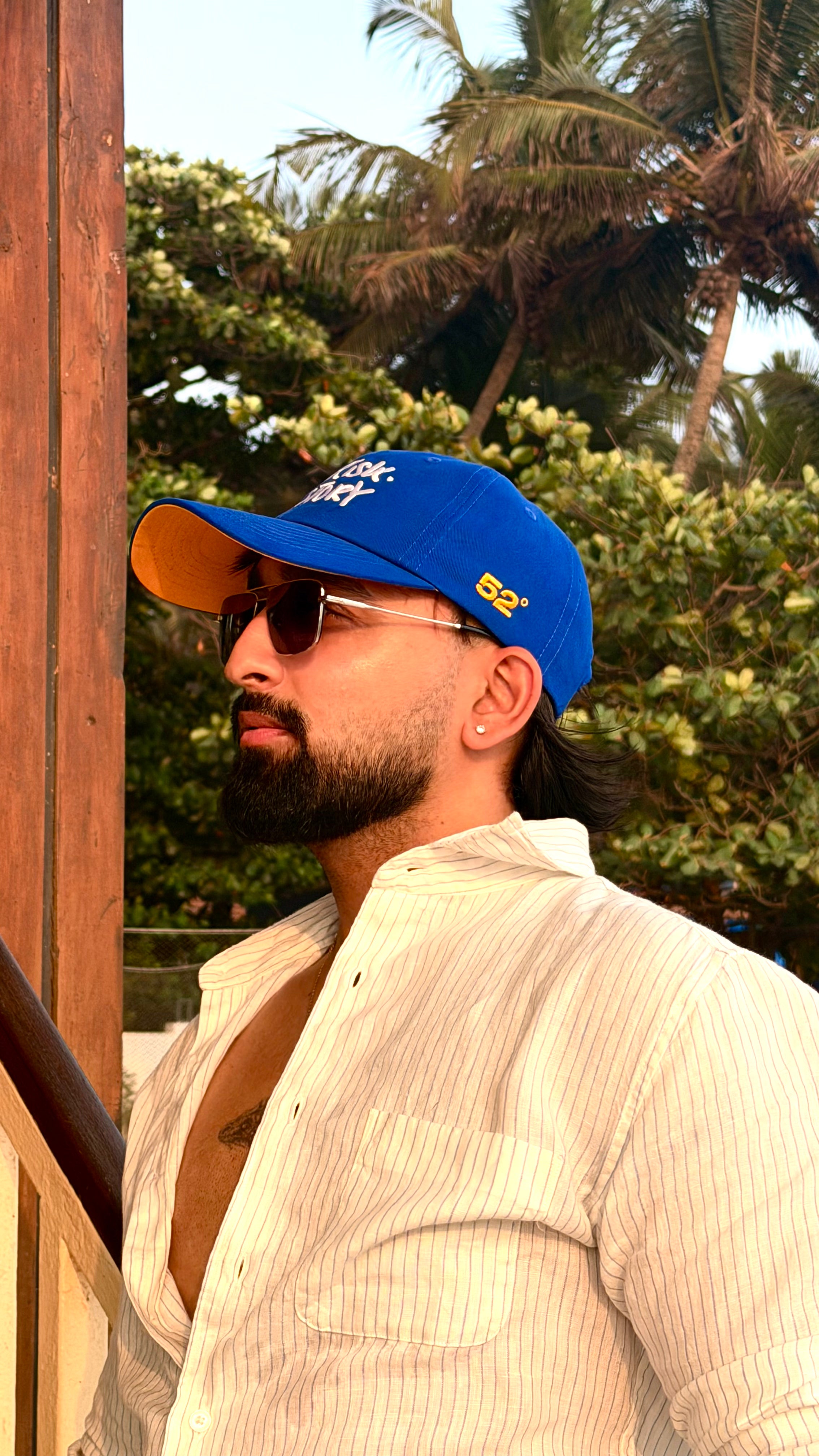 Man wearing a blue cap and sunglasses with palm trees in the background
