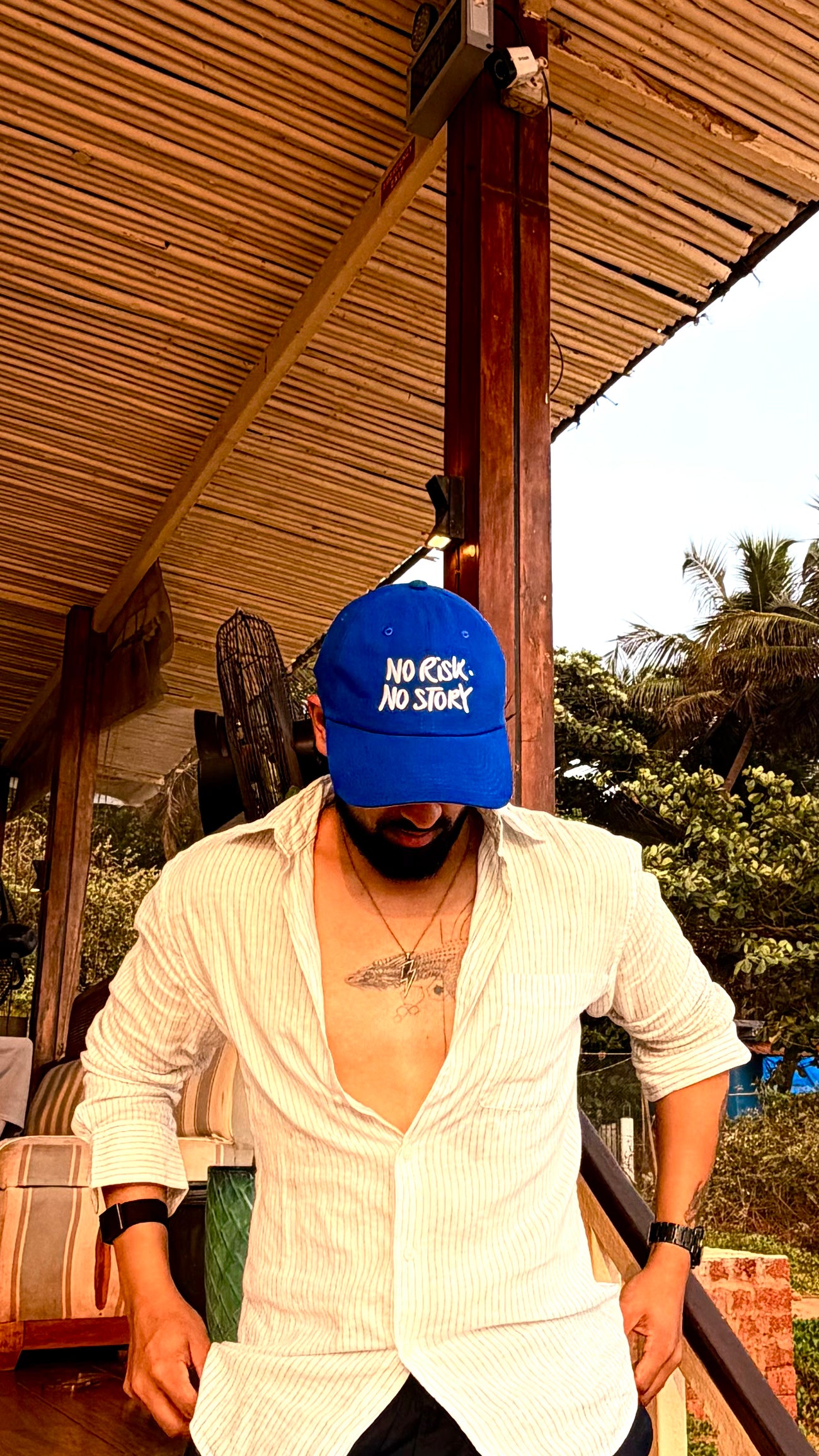 Man wearing a blue cap with text, standing outdoors under a wooden structure.