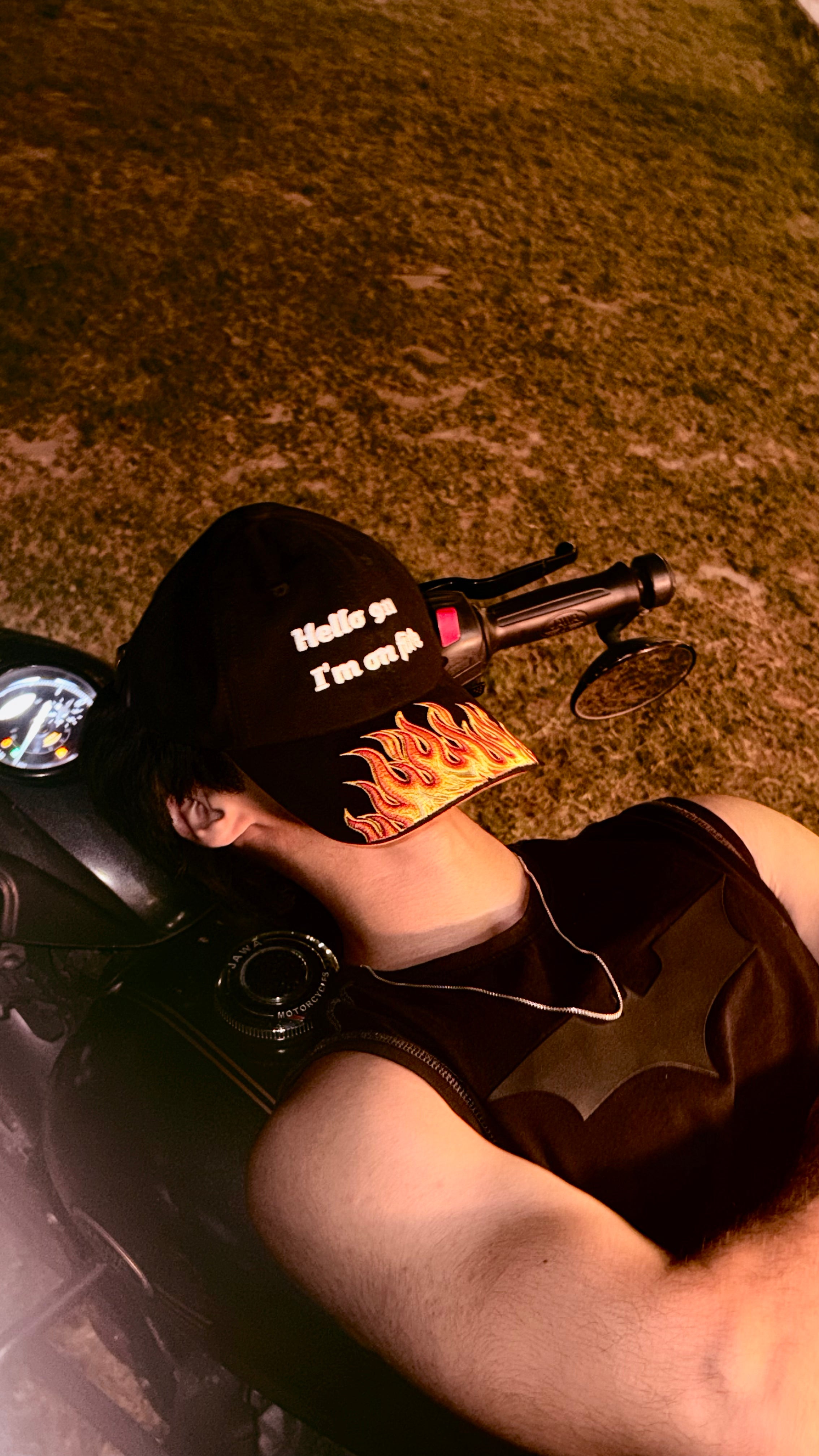 Person wearing a cap with flame design sitting on a motorcycle.