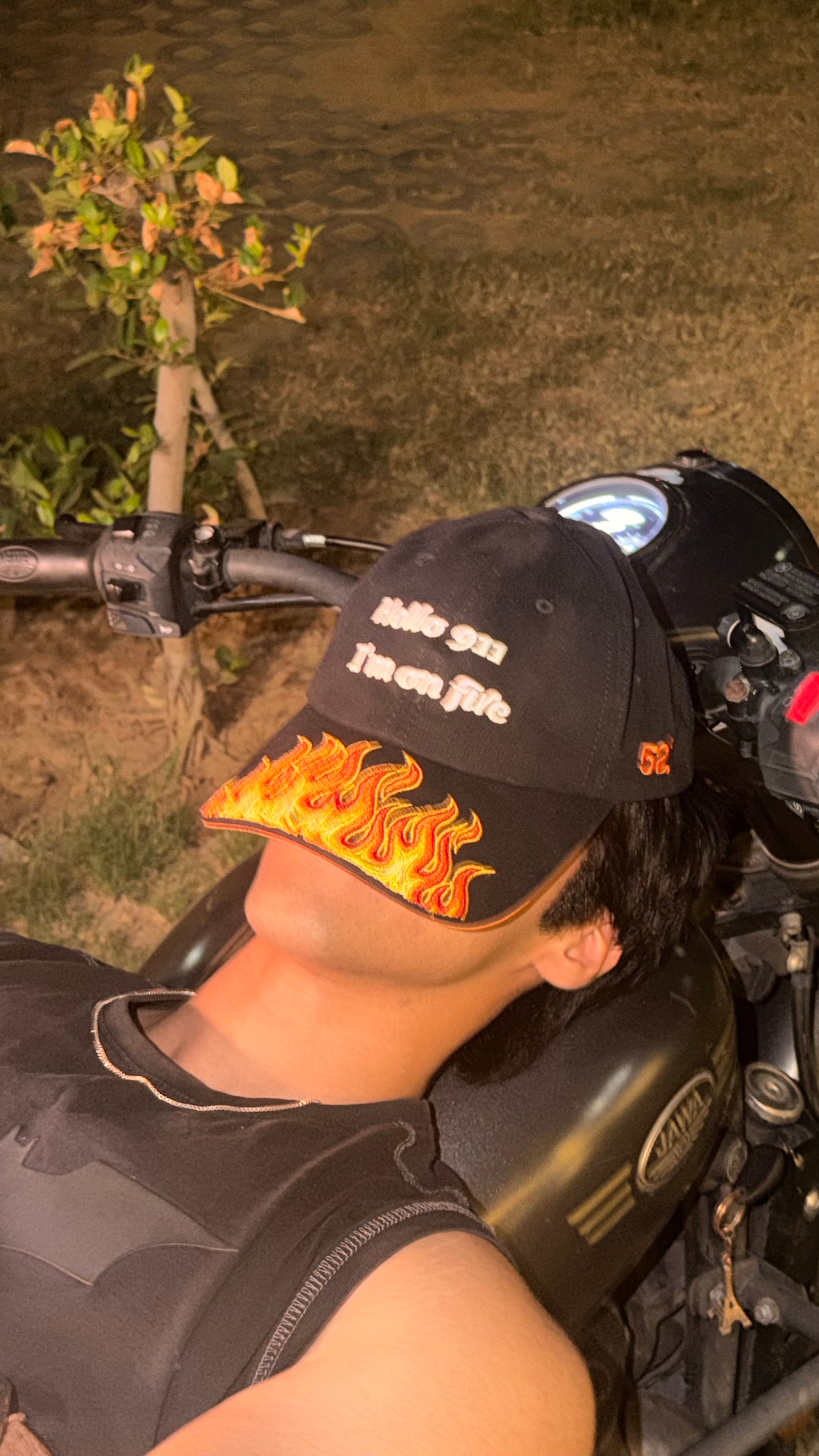 Person wearing a cap with flame design sitting on a motorcycle at night.