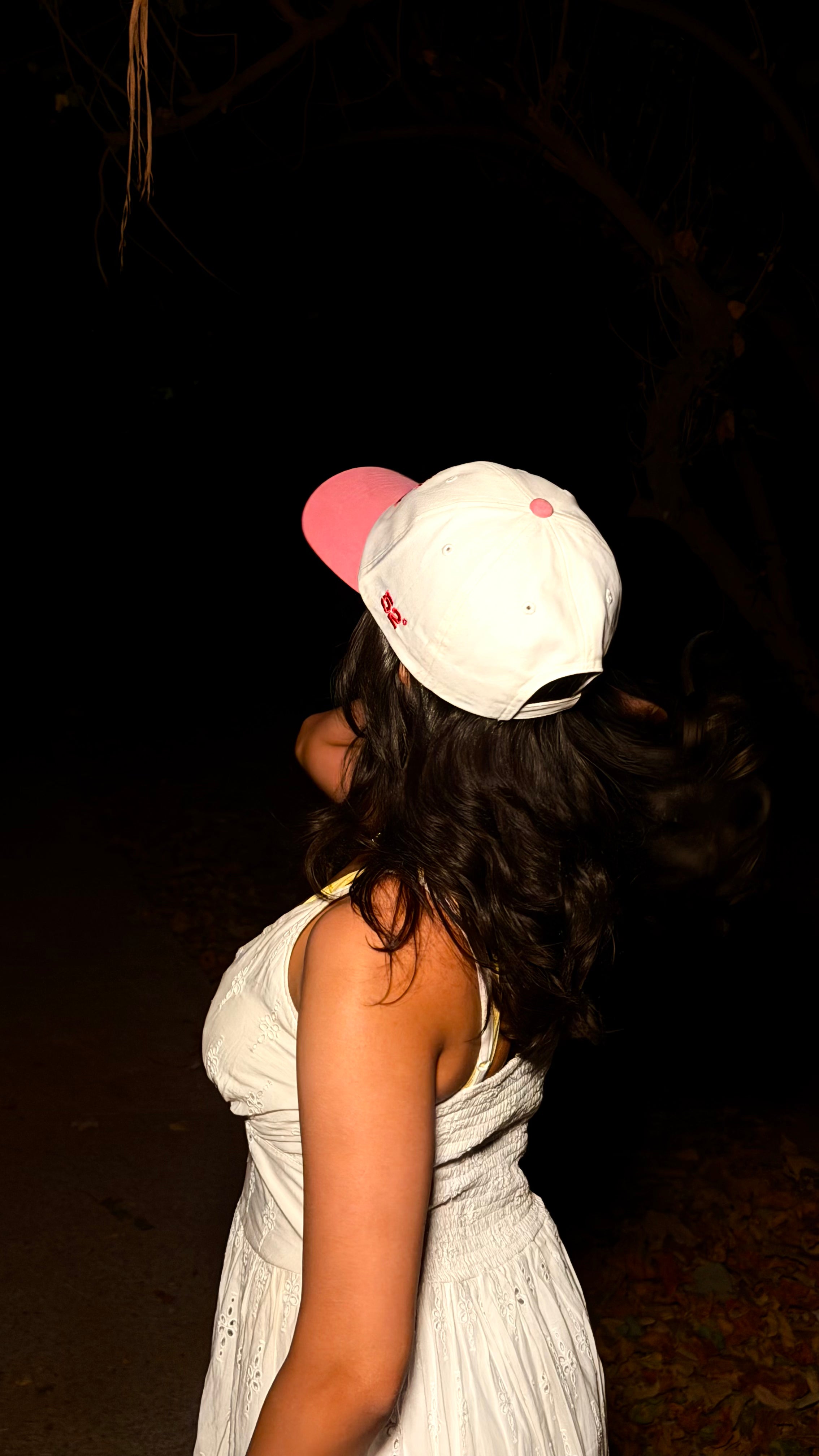 Person wearing a white dress and colorful cap in a dark setting
