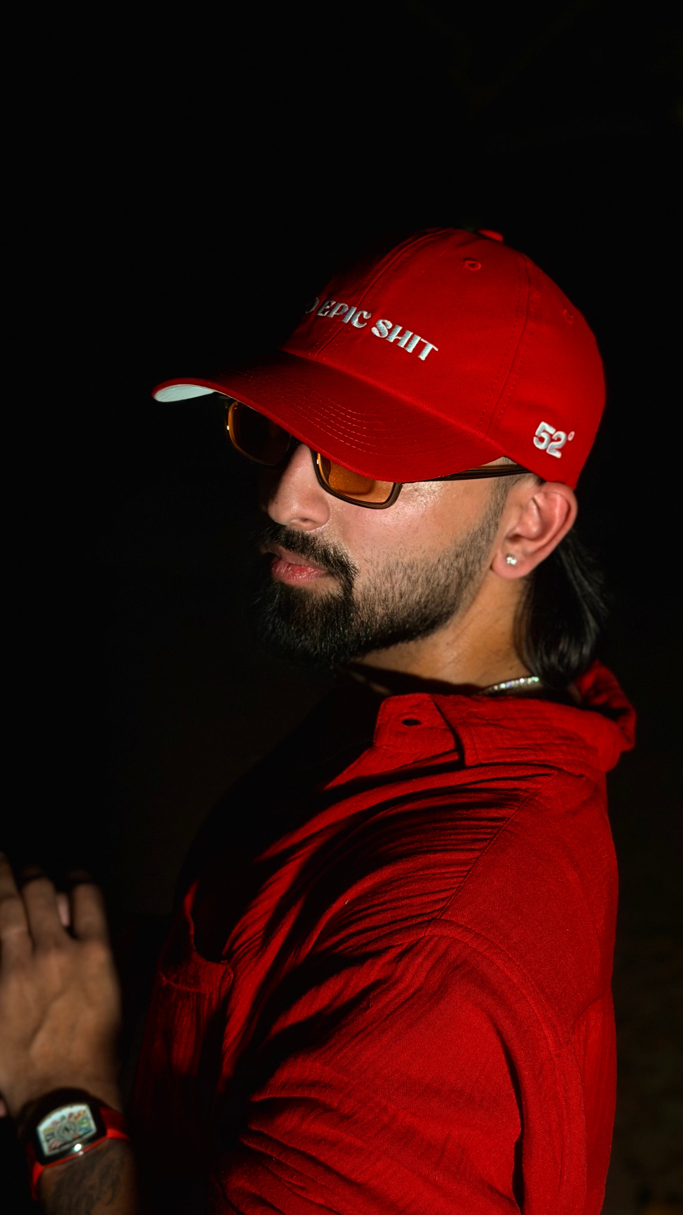 Man wearing a red cap and jacket with sunglasses, against a dark background