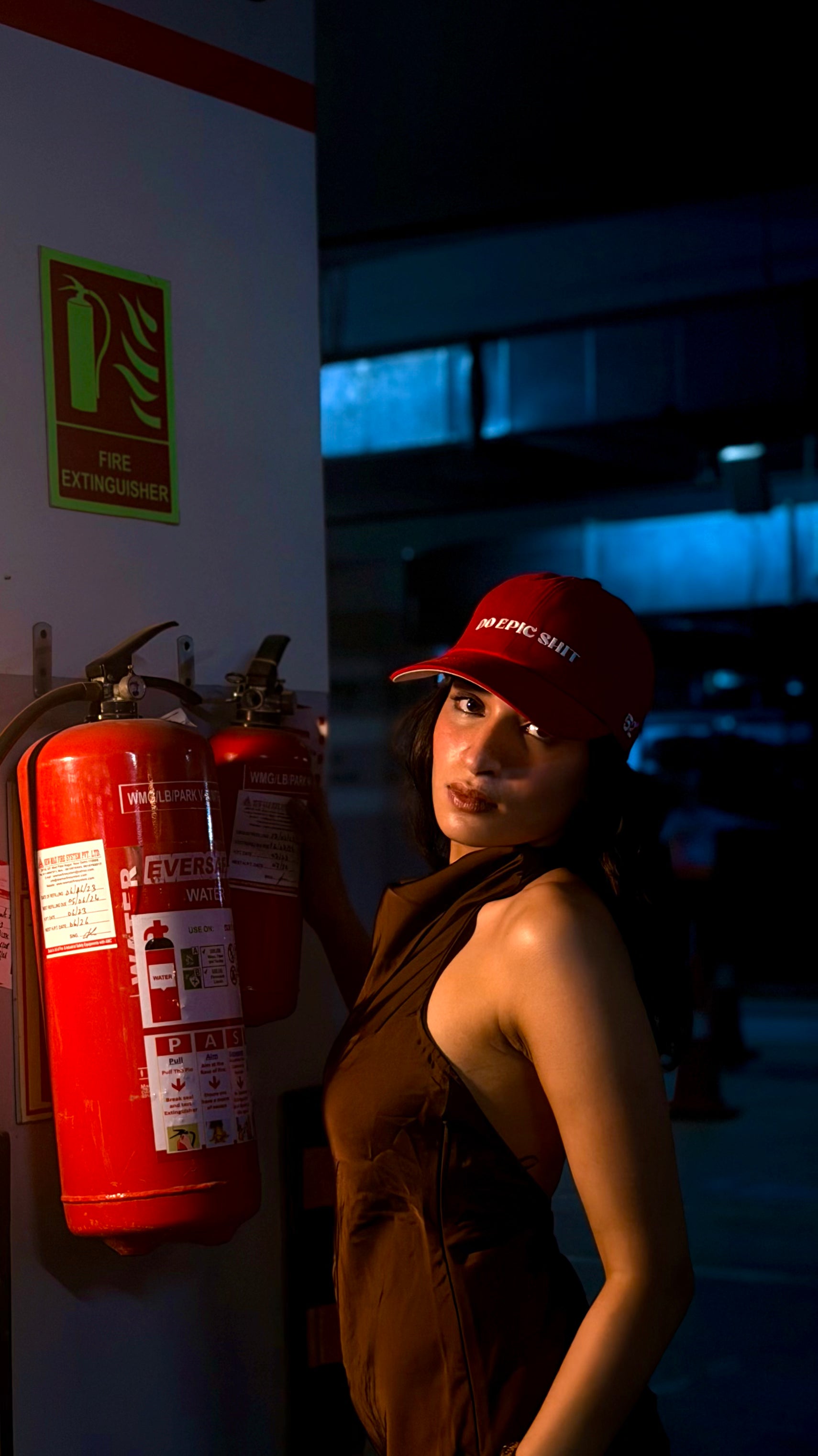 Person wearing a red cap next to fire extinguishers on a wall