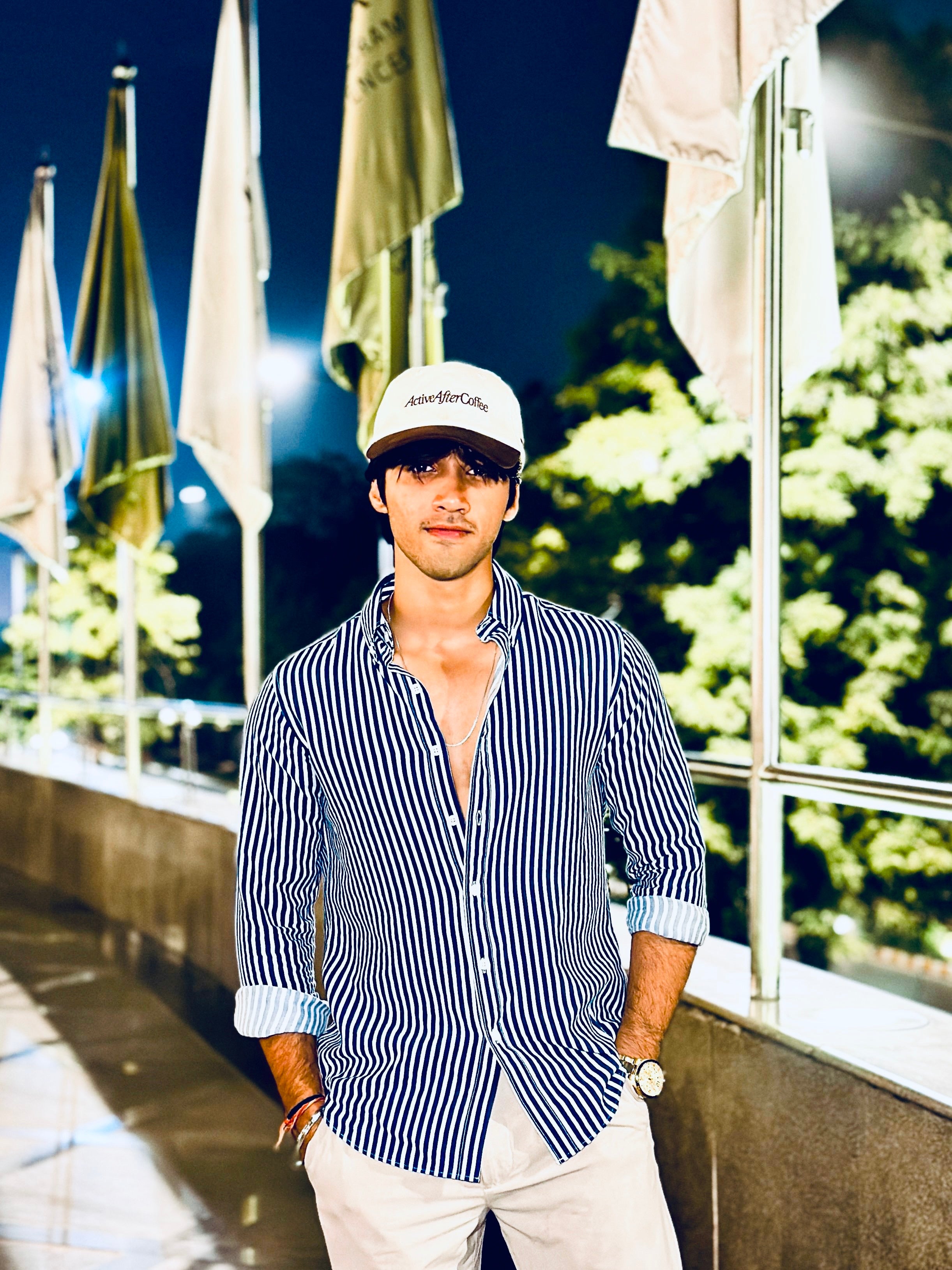 Man wearing a striped shirt and cap standing in front of a building with flags at night.